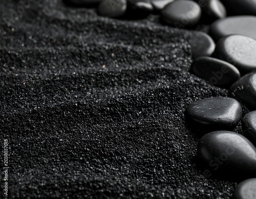 Dark, textured black sand with smooth, dark stones