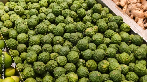 Foto A high-angle view shows a large collection of bumpy kaffir limes displayed in a market metal tray next to fresh ginger roots and standard limes