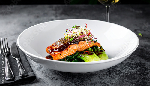 Gourmet Salmon Delight: A succulent piece of pan-seared salmon, glazed with a rich sauce and garnished with sprouts, rests on a bed of wilted greens and avocado.