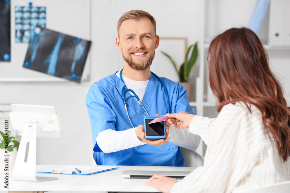 Fototapeta premium Male doctor receiving payment from patient via terminal in clinic
