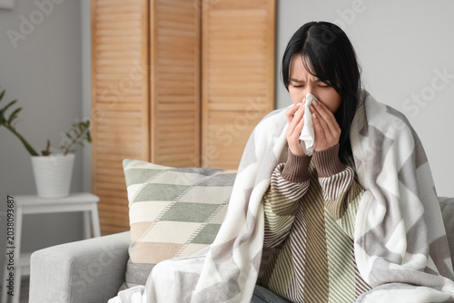 Young woman with plaid and tissue sneezing at home on winter day