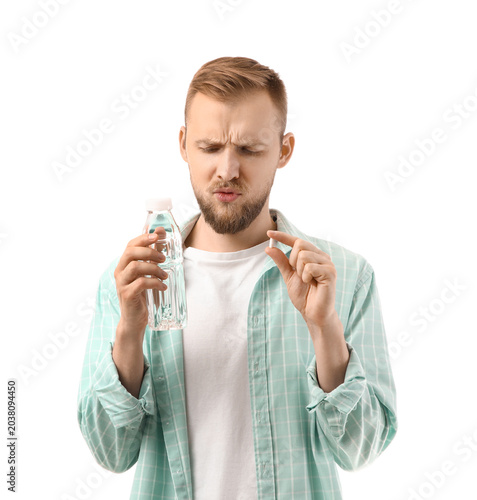 Young man with headache pill and water bottle after party on white background