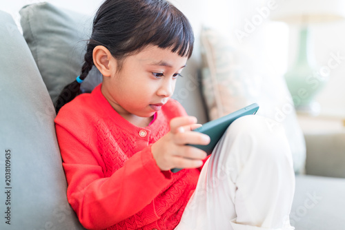 Tableau sur toile Smiling child staring at mobile device while resting on couch