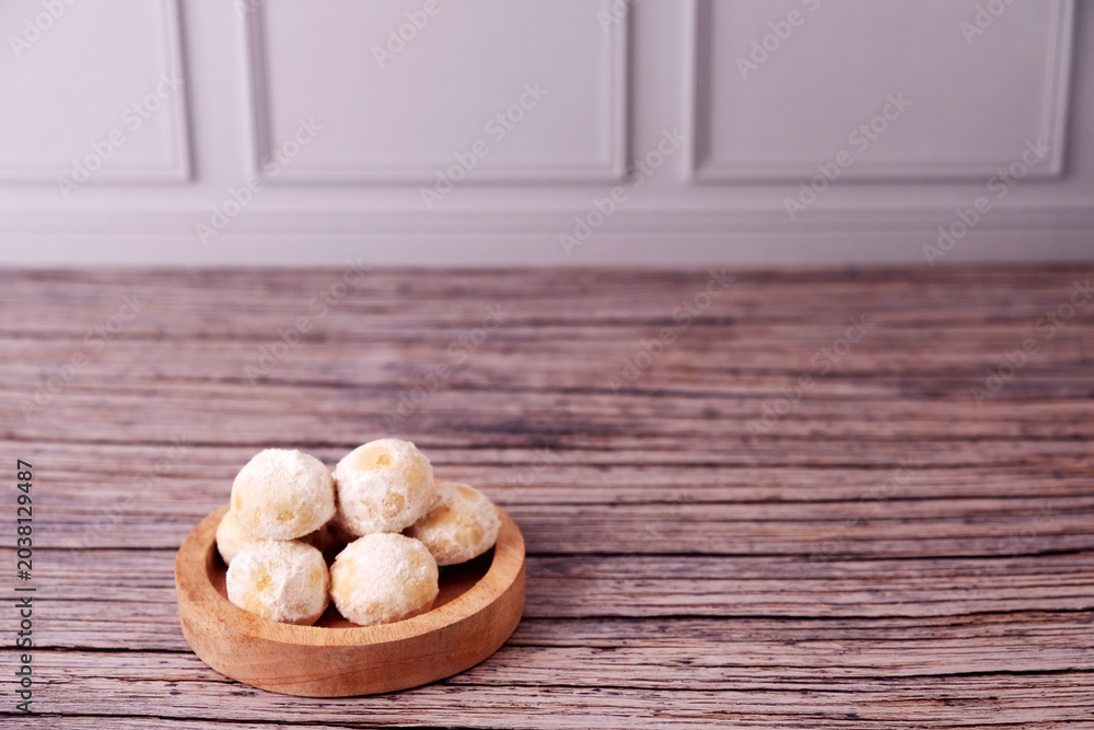 Fototapeta premium Kue Salju Soft, powdered treats rest in a wooden bowl. Warm wood grain adds rustic charm. Minimalist background emphasizes sweet delicacy. Gentle lighting enhances inviting texture. Ideal for food 