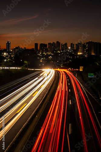 Long exposure shot of car light trails on SP-294 highway with Marilia city buildings in the background during twilight.