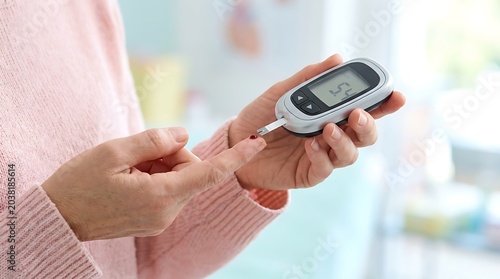 A person's hand holding a glucose meter and a finger pricked for a blood sugar test, indicating diabetes management.