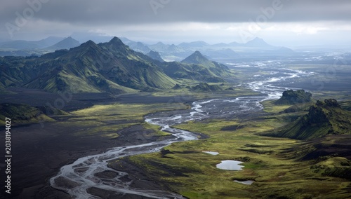 High-angle view of a winding river flowing through a volcanic landscape, surrounded by green hills and mountains