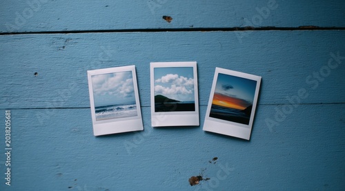 Three instant photos of ocean scenes on a rustic blue wooden table