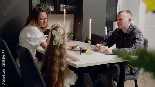 Family gathered around dining table, sharing festive meal with glowing candles, decorated christmas tree illuminating warm holiday moment