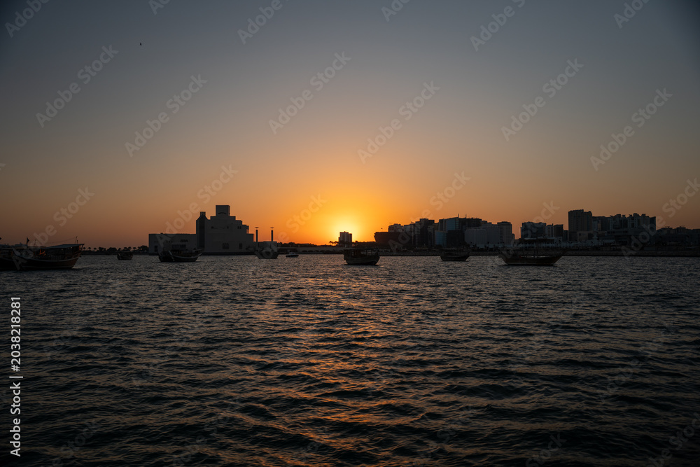 Fototapeta premium Sunset over a city skyline with boats on the water.