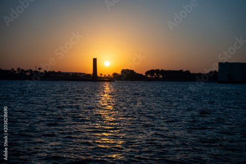 Sunset over water with silhouette of landscape in background.