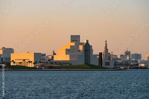 Museum building and mosque tower prominently displayed in sunset light over water.