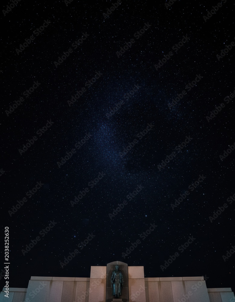 Fototapeta premium Starry night sky with cluster of stars shining over a stark stone memorial at night for astronomy editorial, cinematic storytelling and atmospheric background