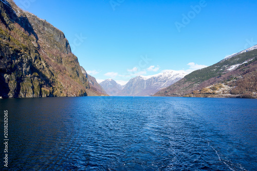 Beautiful panoramic view of the majestic Sognefjord in Norway under a clear blue sky, featuring steep mountains, snow-capped peaks, and deep blue water for travel and adventure themes.