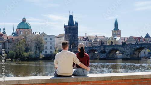 Photos A couple sits together on a stone wall by the Vltava River, gazing at the beautiful cityscape of Prague
