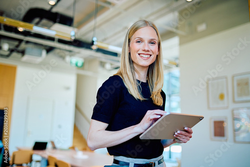 Fotografía Young business woman smiling, using a digital tablet for work in a modern office environment