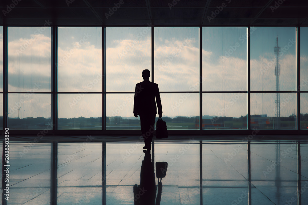 Fototapeta premium Silhouette of a businessman waiting by an airport window with luggage and a city view