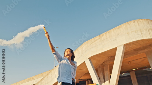 Slika na platnu A skateboarder in adolescence stands beneath a modern concrete structure, holding a torch aloft that emits a small flare