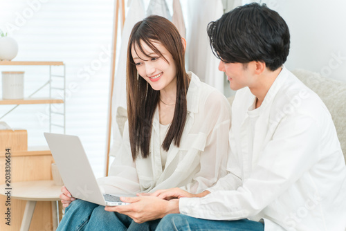 Bild auf Leinwand A young Asian couple sitting on the sofa in their living room, looking at a laptop