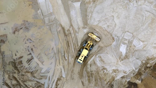 Aerial view shows yellow mining truck on sandy terrain. The truck moves through a large excavation site. Dusty landscape emphasizes industrial scale. Ideal for construction or mining projects