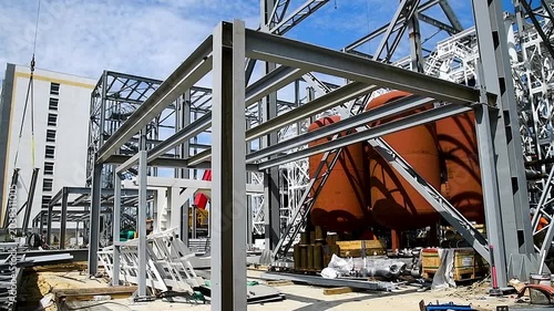 A building structure made of metal beams forming the frame of a building or structure, against a blue sky background.
