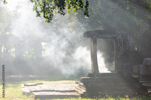 Tableau sur toile Mysterious ancient stone ruins surrounded by morning mist and glowing sunbeams in a peaceful forest