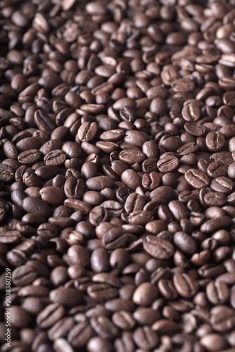 A close-up of dark, freshly roasted coffee beans scattered on a dark background