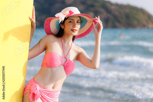 Young Woman In Vibrant Pink Bikini And Sun Hat Posing With Surfboard On Tropical Beach In Rayong Thailand