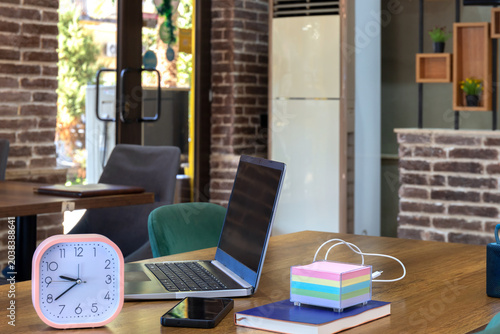Modern office workspace with laptop and desk accessories on wooden table. Business interior with indoor lighting and work equipment. Productivity and remote work concept. Close-up, blurred background.