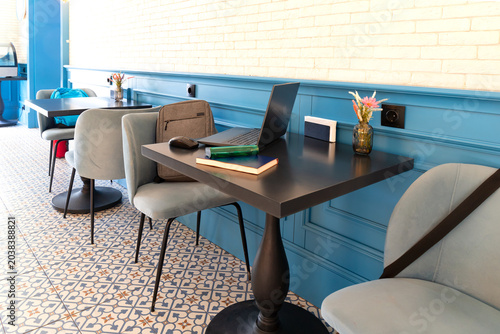 Modern cafe workspace with laptop on black table. Stylish interior with chairs and indoor lighting in cozy business environment. Freelance work and productivity concept. Selective focus.
