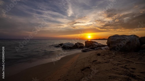 Golden sunset over calm sea with rocky shore and sandy beach