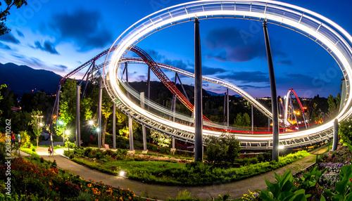 Roller coaster at night with glowing light streaks tracing curves and loops on a sharp steel track against dark sky generative AI