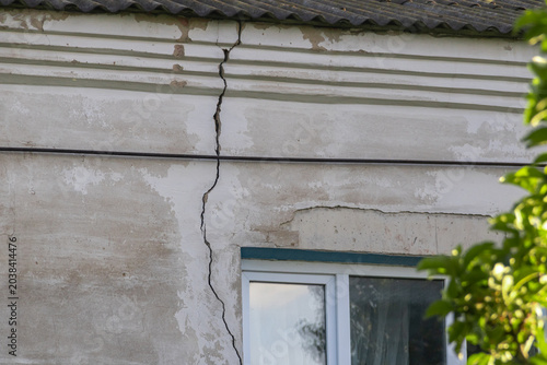 Schilderij op canvas Large deep vertical crack on the old concrete stucco facade of a residential house wall running down from the roof line, building structural failure and property insurance concept