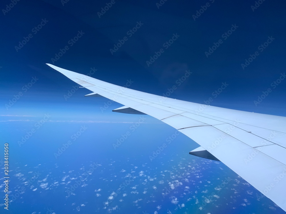 Fototapeta premium White Airplane Wing Flying High Above Blue Ocean and Scattered Clouds