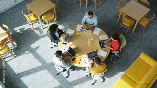 People sit around a table working on laptops in a bright office space
