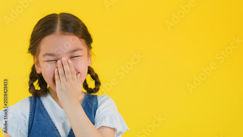Tableau sur toile Young Asian Girl Laughing and Covering Her Mouth on Yellow Background