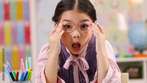фотографія Surprised Asian Schoolgirl Adjusting Pink Glasses in a Colorful Classroom
