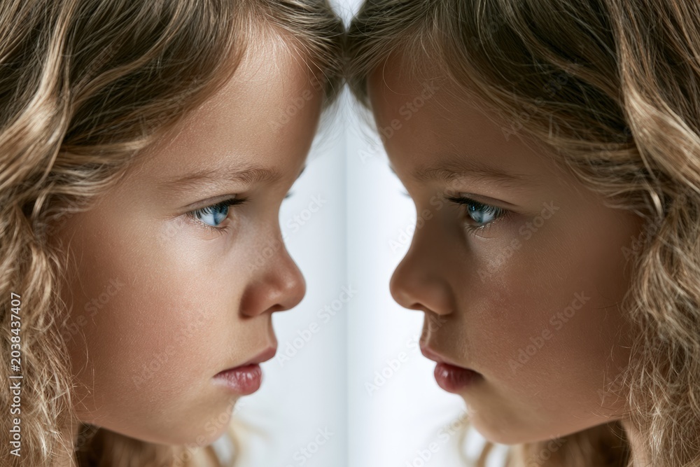 Fototapeta premium Close-up of young girl looking at her reflection with serious expression