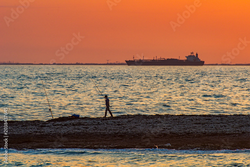 Photos Fisherman walking on beach casting rod at sunset