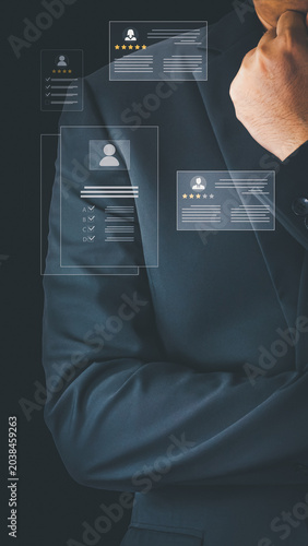 A businessman in a suit analyzes digital candidate profiles for recruitment. The virtual interface displays star ratings and resumes on a black background during business hours.