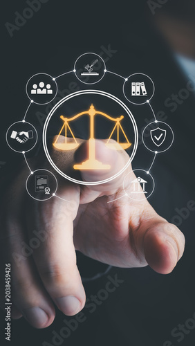 A businessman's finger touches a glowing virtual scale of justice on a digital interface. It includes legal icons like a gavel and documents on a dark background for law services.