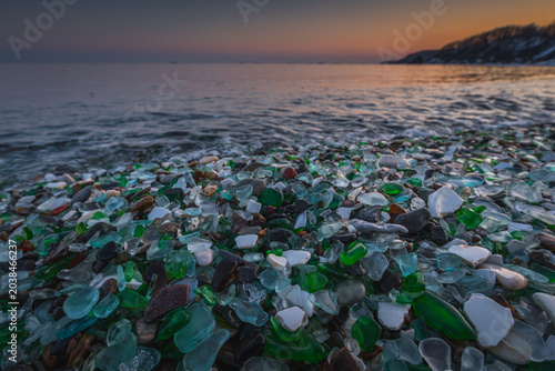 Canvas Print Colorful sea glass pieces scattered on a rocky beach at sunset, with calm waves