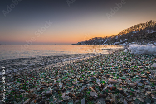 Canvas Print Scenic view of a beach covered in colorful sea glass and pebbles at sunset, with
