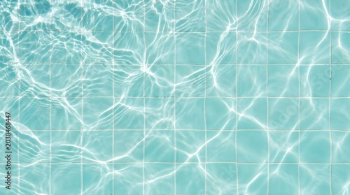 Bright sunlight creates beautiful shimmering caustic patterns on the surface of clear turquoise water covering square tiles in this high angle overhead shot of a pool