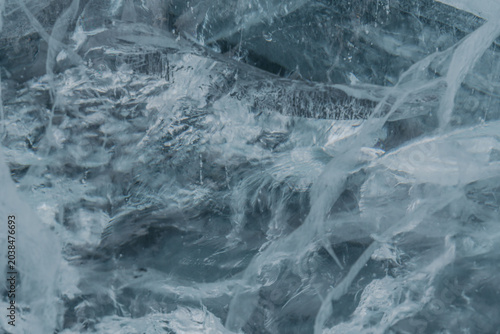 Close-up view of textured ice surface with intricate patterns and layers, showcasing natural formations and reflections in a cool color palette