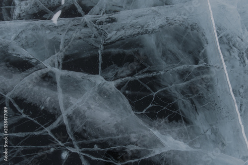 Close-up view of cracked ice surface with intricate patterns and textures, showcasing a mix of clear and opaque areas against a dark background