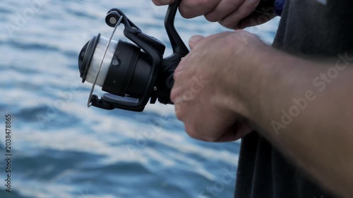 Close up of young fisherman hands using a spinning reel while fishing peacefully in nature during a calm outdoor recreational moment.