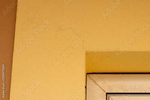 Schilderij op canvas Subtle hairline cracks appear on a textured yellow exterior wall near a window f