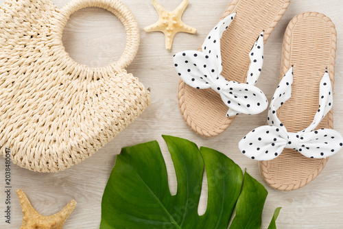 Straw bag with sandals on wooden background, top view