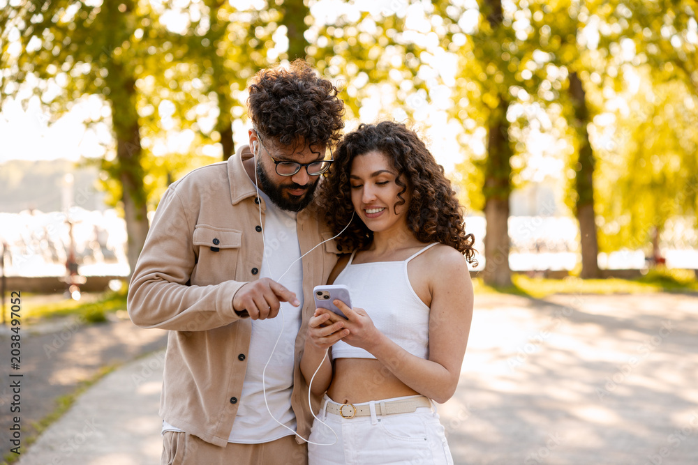 Fototapeta premium Young couple sharing earphones for music on smartphone